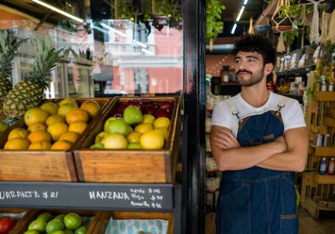 Latin American man working at a local supermarket and waiting for clients at the door - essential services concepts